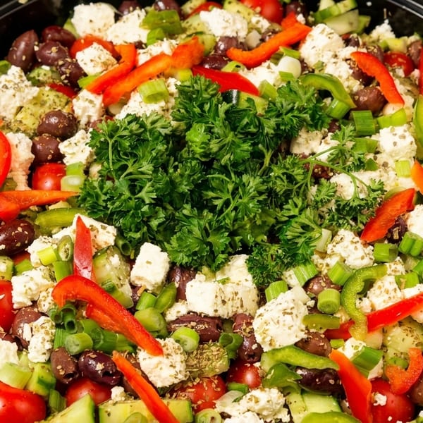 Vibrant Greek salad with feta, olives, cucumbers, tomatoes, peppers, and parsley in a black bowl.