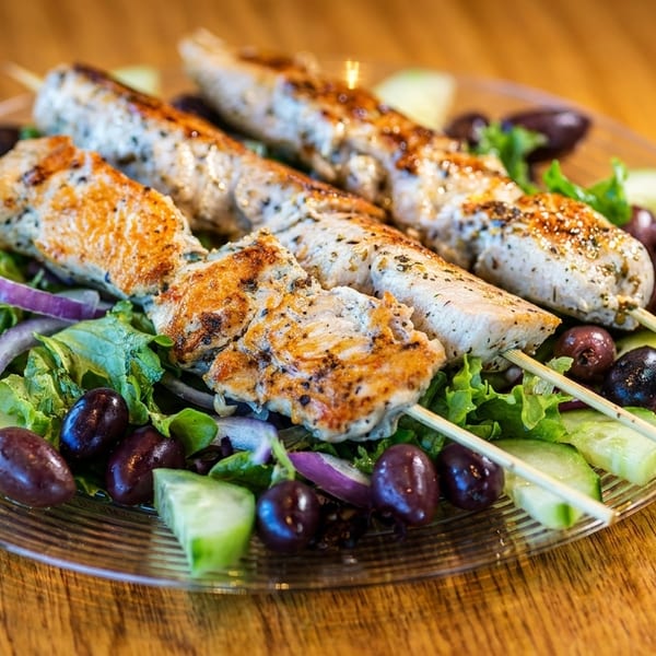 Grilled chicken skewers on a fresh salad with olives, cucumbers, and red onions.
