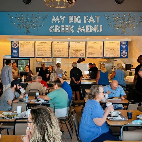 Customers dining and ordering at a busy "My Big Fat Greek Menu" restaurant.