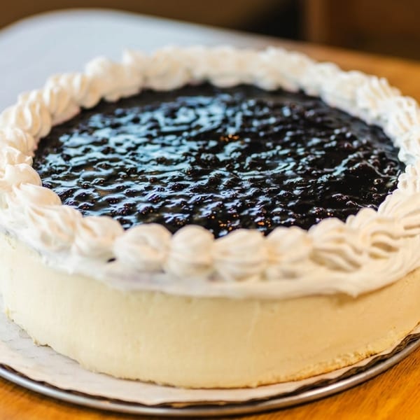 Whole blueberry cheesecake with whipped cream border on a plate on a wooden table.